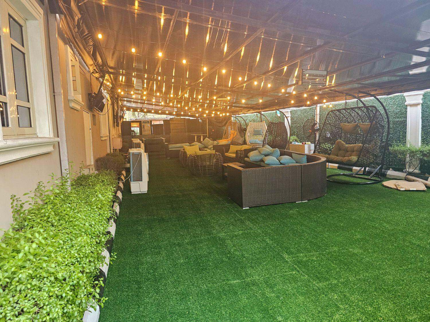 The SafeHouse lawn by day: turf, lounge seating and hanging chairs under the canopy